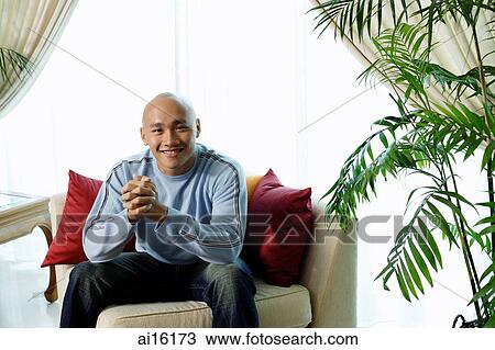 Man sitting on sofa in living room, smiling at camera View Large Photo Image Stock Image - Man sitting on sofa in living room, smiling at camera. Fotosearch