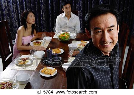 Man smiling at camera, people in the background sitting around table View Large Photo Image Picture - Man smiling at camera, people in the background sitting around table. Fotosearch