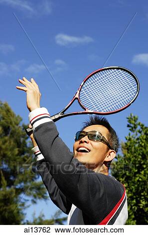 Stock Image - Man wearing sunglasses and holding tennis racket. Fotosearch