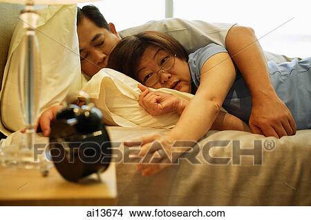 Mature couple sleeping in bedroom, woman reaching for alarm clock View Large Photo Image Picture - Mature couple sleeping in bedroom, woman reaching for alarm clock. Fotosearch
