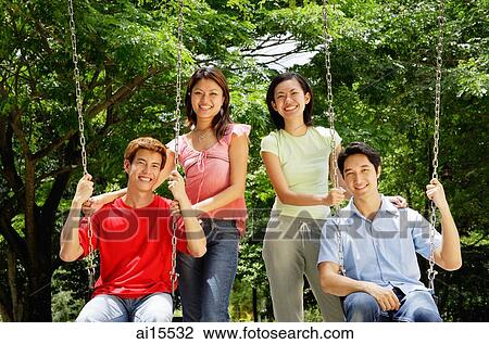 Stock Image - Men on swings, women standing next to them. Fotosearch