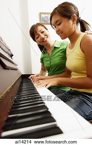 Picture - Mother and daughter sitting side by side in front of piano, mother with hand on daughter's shoulder. Fotosearch