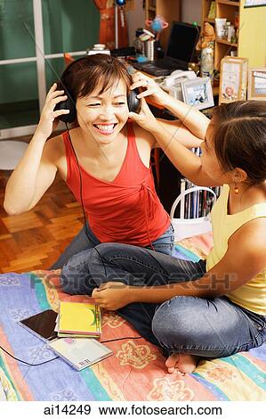Mother and daughter sitting side by side, mother listening to headphones View Large Photo Image Stock Photo - Mother and daughter sitting side by side, mother listening to headphones. Fotosearch