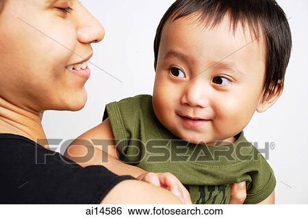 Stock Photograph - Mother carrying baby boy, both smiling. Fotosearch