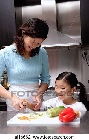 Stock Image - Mother cutting vegetables, daughter helping her. Fotosearch