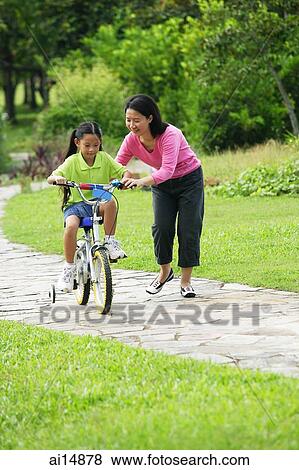 Mother guiding daughter on bicycle View Large Photo Image Stock Photo - Mother guiding daughter on bicycle. Fotosearch