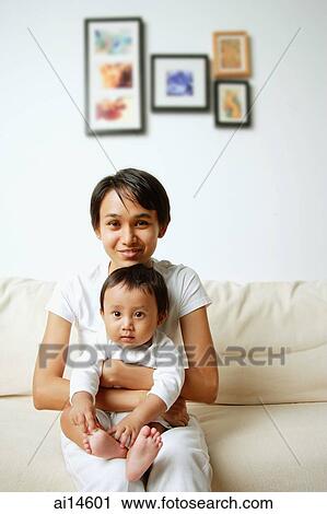 Stock Image - Mother with baby boy, sitting on sofa, portrait. Fotosearch