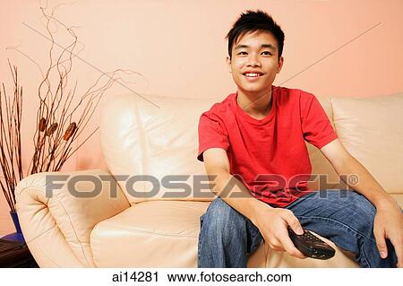 Teenage boy sitting on sofa, holding remote control View Large Photo Image Stock Image - Teenage boy sitting on sofa, holding remote control. Fotosearch
