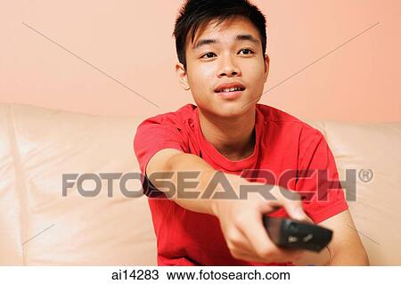 Teenage boy sitting on sofa, holding remote control forward View Large Photo Image Stock Image - Teenage boy sitting on sofa, holding remote control forward. Fotosearch