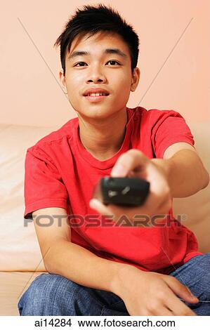 Teenage boy sitting on sofa, pointing remote control towards camera View Large Photo Image Picture - Teenage boy sitting on sofa, pointing remote control towards camera. Fotosearch