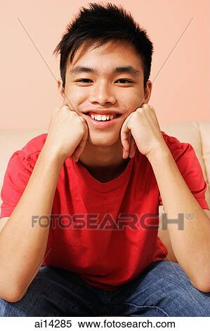Stock Photography - Teenage boy sitting with hands on chin, looking at camera. Fotosearch