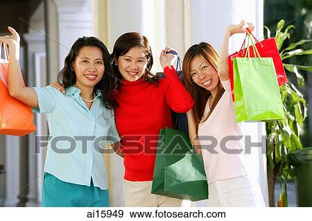 Stock Photo - Three women carrying shopping bags, smiling at camera, portrait. Fotosearch