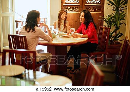 Stock Image - Three women having lunch at restaurant. Fotosearch
