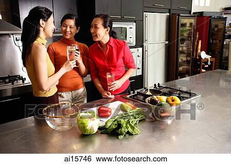 Stock Photograph - Three women in kitchen, holding wine glasses, talking. Fotosearch