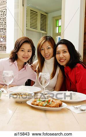 Stock Image - Three women sitting at restaurant table, smiling. Fotosearch