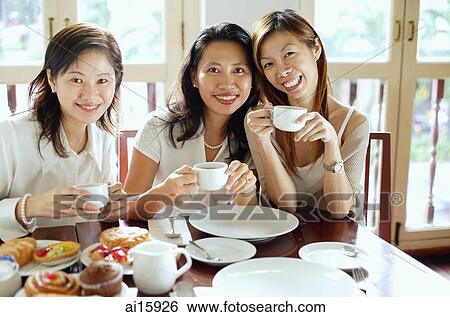 Three women sitting side by side in cafe, smiling at camera View Large Photo Image Stock Photograph - Three women sitting side by side in cafe, smiling at camera. Fotosearch