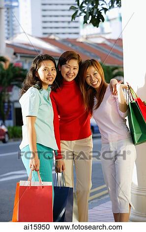Three women standing, carrying shopping bags, smiling at camera View Large Photo Image Stock Image - Three women standing, carrying shopping bags, smiling at camera. Fotosearch