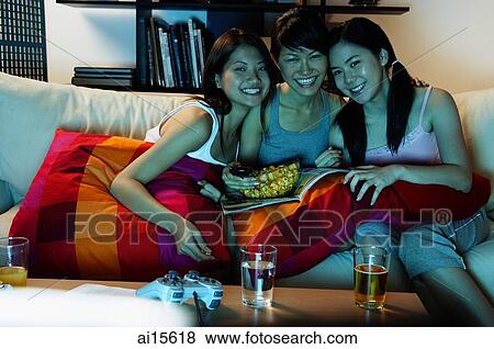 Three young women in living room, sitting on sofa, smiling at camera View Large Photo Image Stock Photo - Three young women in living room, sitting on sofa, smiling at camera. Fotosearch