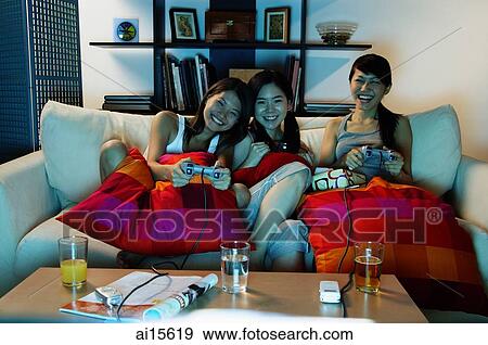 Three young women in living room, playing video games View Large Photo Image Stock Photo - Three young women in living room, playing video games. Fotosearch