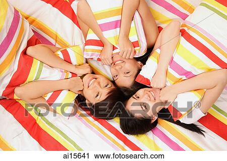 Three young women lying on bed, hugging pillows, looking up at camera View Large Photo Image Stock Image - Three young women lying on bed, hugging pillows, looking up at camera. Fotosearch