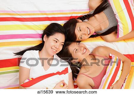 Three young women lying on bed, smiling View Large Photo Image Stock Photo - Three young women lying on bed, smiling. Fotosearch