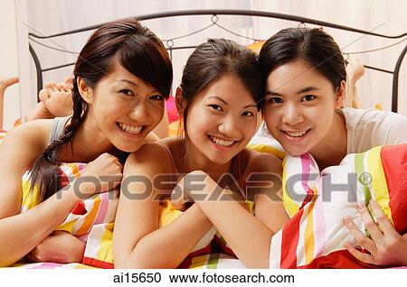 Three young women lying side by side on bed, smiling at camera View Large Photo Image Stock Image - Three young women lying side by side on bed, smiling at camera. Fotosearch