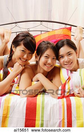 Three young women lying side by side on bed, looking at camera, smiling View Large Photo Image Stock Image - Three young women lying side by side on bed, looking at camera, smiling. Fotosearch