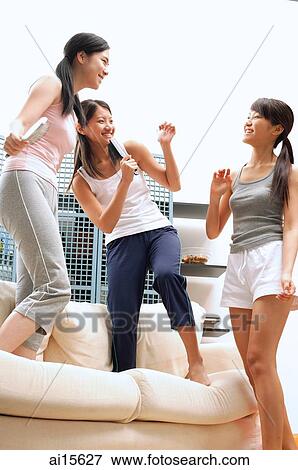 Three young women standing on sofa, holding hairbrushes View Large Photo Image Stock Photo - Three young women standing on sofa, holding hairbrushes. Fotosearch