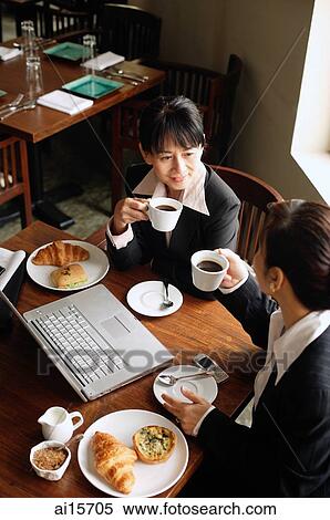 Stock Photography - Two businesswomen at cafe, drinking coffee, laptop on table. Fotosearch