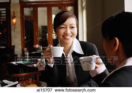 Stock Photo - Two businesswomen at cafe, holding cups, smiling. Fotosearch