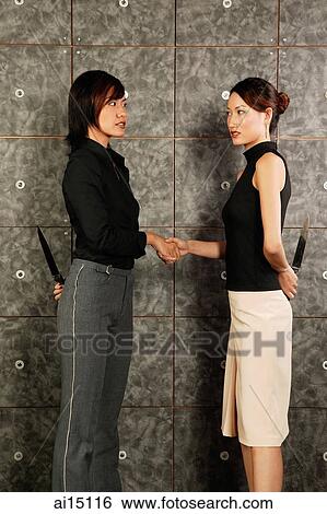 Two female executives face to face, shaking hands, holding knives behind their backs View Large Photo Image Stock Photograph - Two female executives face to face, shaking hands, holding knives behind their backs. Fotosearch