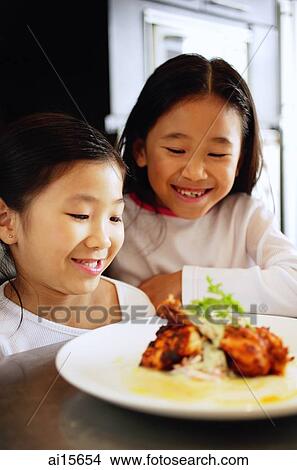 Two girls looking at a plate of food, smiling View Large Photo Image Picture - Two girls looking at a plate of food, smiling. Fotosearch