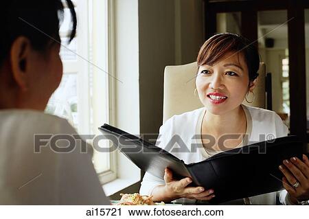 Two women at restaurant, one holding menu View Large Photo Image Stock Image - Two women at restaurant, one holding menu. Fotosearch