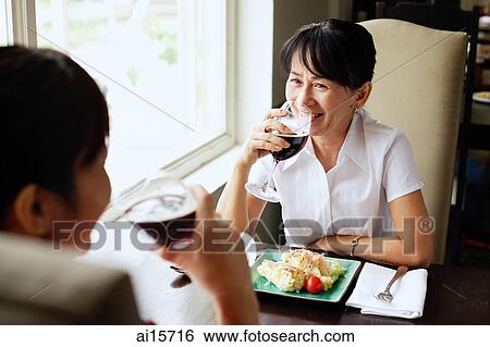 Two women at restaurant, sitting face to face, drinking wine, food on the table View Large Photo Image Stock Photograph - Two women at restaurant, sitting face to face, drinking wine, food on the table. Fotosearch