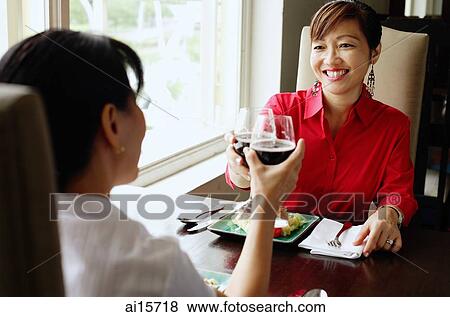 Two women at restaurant, toasting with wine glasses View Large Photo Image Stock Photo - Two women at restaurant, toasting with wine glasses. Fotosearch