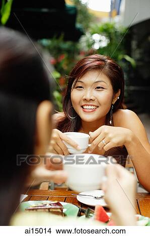 Picture - Two women facing each other holding coffee cups.. Fotosearch