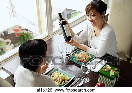 Two women in restaurant having lunch, one woman holding bottle of wine View Large Photo Image Stock Photograph - Two women in restaurant having lunch, one woman holding bottle of wine. Fotosearch