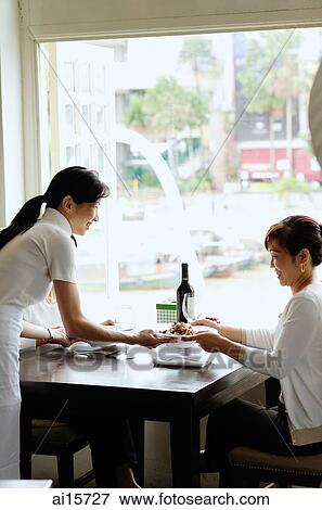 Stock Photo - Two women in restaurant, waitress serving food. Fotosearch