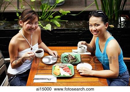 Two women sitting at table, having coffee and fruits, looking up at camera View Large Photo Image Stock Image - Two women sitting at table, having coffee and fruits, looking up at camera. Fotosearch
