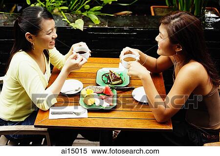Stock Photography - Two women sitting at table, having coffee and fruits. Fotosearch