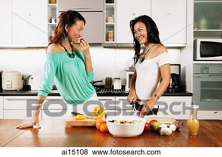 Stock Photo - Two women standing in kitchen, one chopping vegetables. Fotosearch