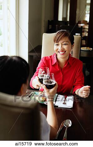 Two women toasting with wine glasses, sitting in restaurant View Large Photo Image Stock Photo - Two women toasting with wine glasses, sitting in restaurant. Fotosearch
