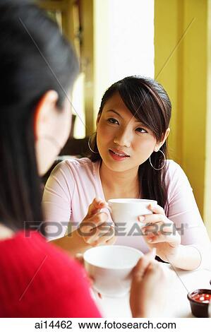 Stock Image - Two young women at cafe, having coffee, over the shoulder view. Fotosearch