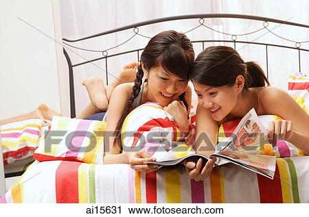 Two young women lying on bed, going through magazine View Large Photo Image Stock Image - Two young women lying on bed, going through magazine. Fotosearch