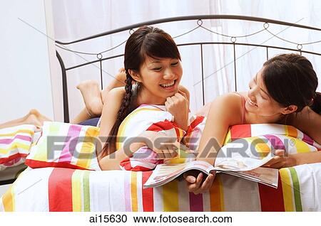 Two young women lying on bed, looking at magazine View Large Photo Image Stock Image - Two young women lying on bed, looking at magazine. Fotosearch