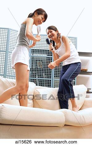 Two young women standing on sofa, holding hairbrushes View Large Photo Image Stock Photograph - Two young women standing on sofa, holding hairbrushes. Fotosearch