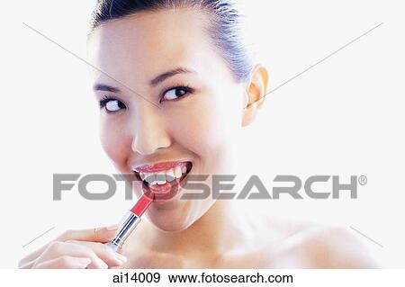 Stock Photo - Woman applying lipstick, looking away, smiling. Fotosearch