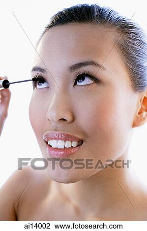 Stock Image - Woman applying mascara, looking up. Fotosearch