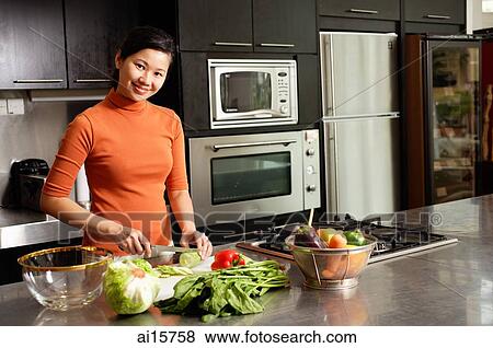 Woman cutting vegetables in kitchen, smiling at camera, portrait View Large Photo Image Stock Photo - Woman cutting vegetables in kitchen, smiling at camera, portrait. Fotosearch