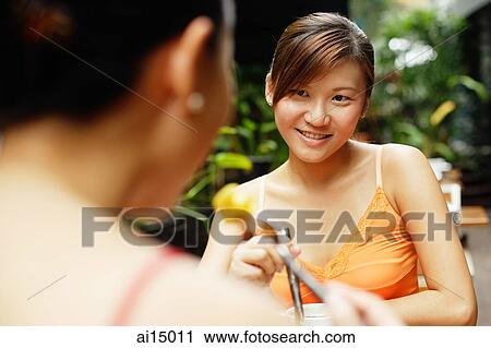 Stock Image - Woman eating, facing another person. Fotosearch